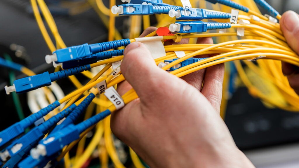 Fiber Optic Installation in Qatar showing technician handling yellow cables with blue connectors.