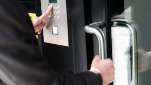 Person in business attire entering an access code on a keypad door entry system while opening a glass office door